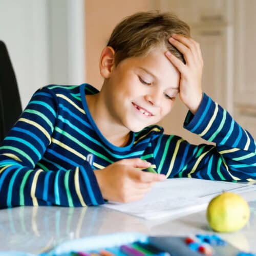 Hard-working happy school kid boy making homework during quarantine time from corona pandemic disease. Healthy child writing with pen, staying at home. Homeschooling concept Hard-working happy school kid boy making homework during quarantine time from corona pandemic disease. Healthy child writing with pen, staying at home. Homeschooling concept.
