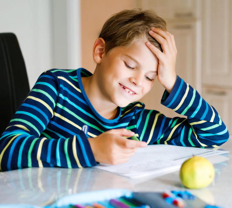 Hard-working happy school kid boy making homework during quarantine time from corona pandemic disease. Healthy child writing with pen, staying at home. Homeschooling concept.