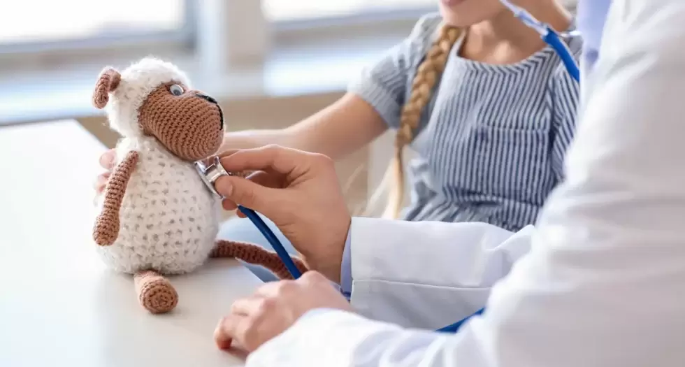 Un médecin prête son stéthoscope à un enfant pour lui expliquer comment il entend son coeur, en le testant sur une peluche