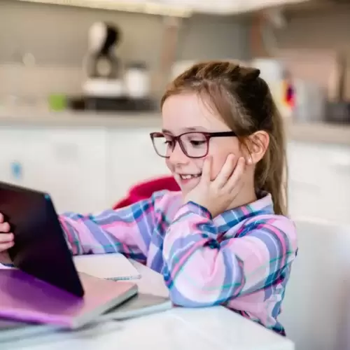AdobeStock_276428980-scaled Une petite fille suit un cours d'une école en ligne. Elle a l'air heureuse.